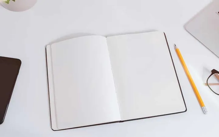 A notebook, phone and glasses laid out on a white desk